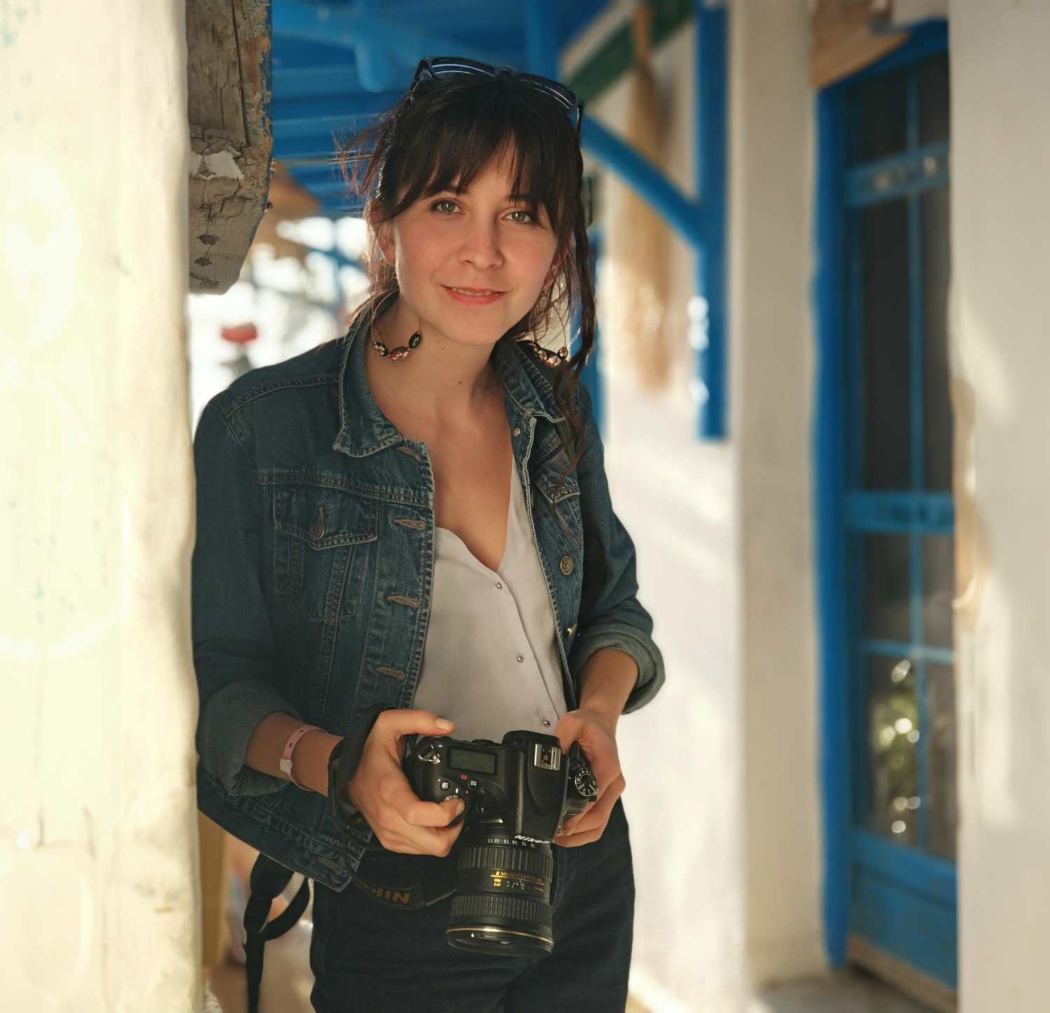 Smiling artist is holding digital photo camera, near neutral clay wall and blue framed door.