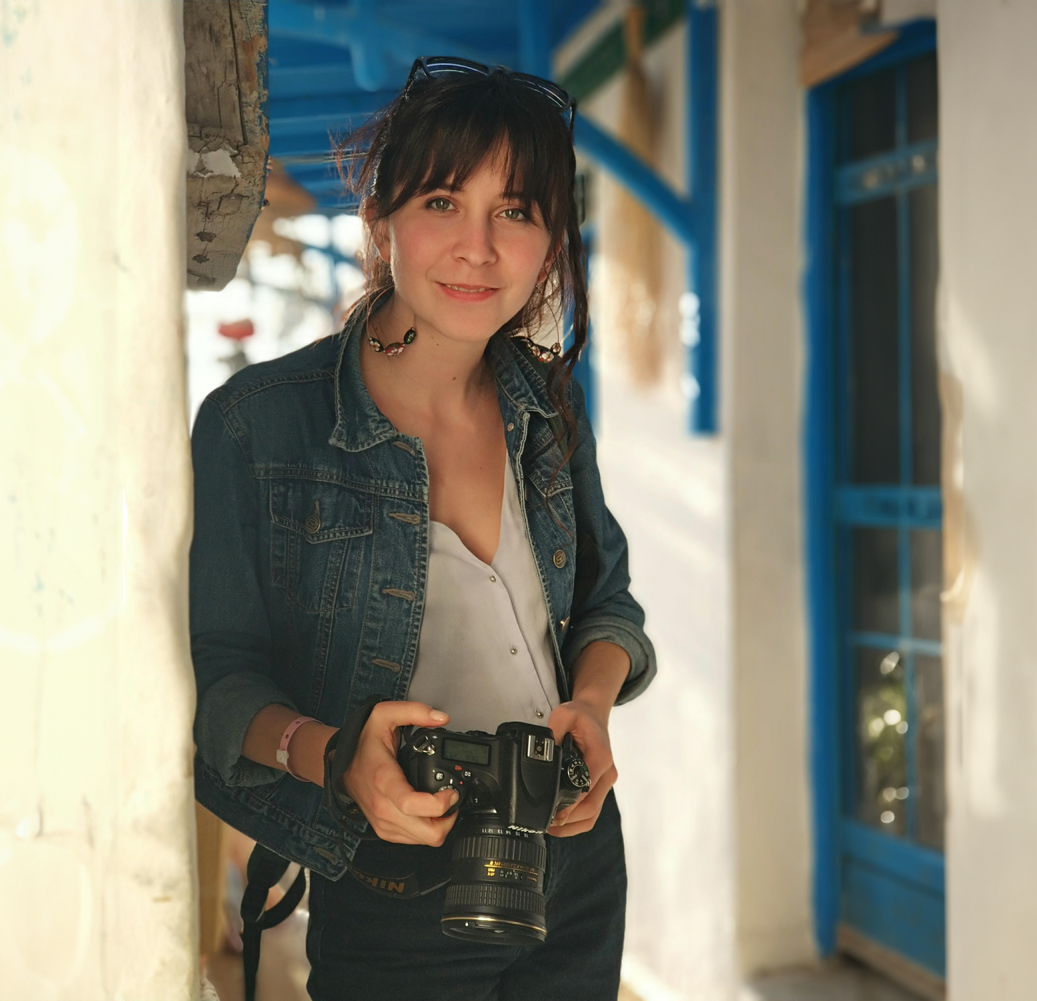 Smiling artist is holding digital photo camera, near neutral clay wall and blue framed door. 